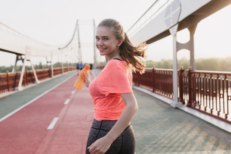 portrait-from-back-of-spectacular-white-girl-running-with-bottle-of-water-joyful-female-runner-in-pink-t-shirt-looking-over-shoulder
